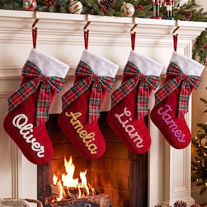 May include: Four red quilted Christmas stockings with white cuffs and plaid bows hanging from gold hooks. Each stocking features a personalized name embroidered in script: Oliver in white, Amelia in gold, Liam in pink, and James in purple.