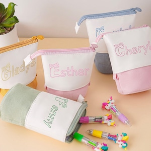 Può includere: Astucci personalizzati in giallo, rosa, blu e verde. Ogni astuccio presenta un nome ricamato in un colore coordinato. Sono presenti anche diverse penne a forma di unicorno.