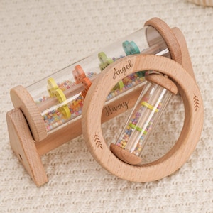 Peut inclure: Hochets en bois pour bébés avec des tubes transparents remplis de perles colorées. Le hochet a une poignée circulaire avec les noms "Angel" et "Harry" gravés. Conçu pour les bébés et les tout-petits.
