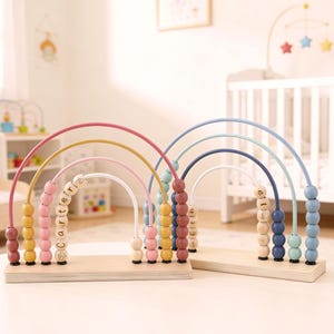 May include: Two wooden rainbow bead mazes on a light wood base. One has pink, yellow, and white arches with the name "Carterly" spelled out. The other has blue, green, and white arches. The toys are in a nursery setting.