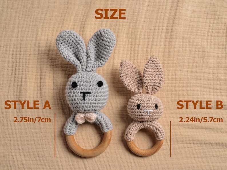 May include: Two crochet bunny rattles, Style A in gray with a pink bow tie, and Style B in tan. Each bunny has a wooden ring base. Style A measures 2.75 inches (7cm) and Style B measures 2.24 inches (5.7cm).