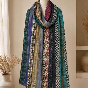 May include: A long rectangular scarf featuring a vertical patchwork design with various patterns and colors including deep green, burgundy, black, gold, and teal. The fabric displays a mix of geometric, floral, and abstract prints in a layered style.