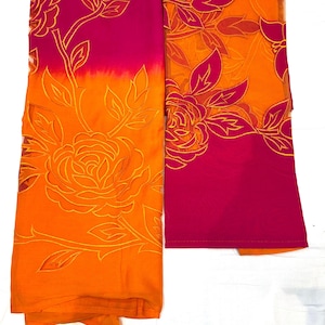 May include: Two pieces of fabric, one folded, in shades of orange and pink. The fabric features a floral design with a rose and leaves in a lighter orange color. The background is white.