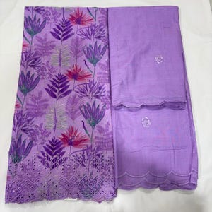 May include: A two-piece fabric set in light purple. One piece features a vibrant floral and fern print in shades of purple, pink, and green with a scalloped eyelet border. The second piece is a solid light purple fabric with small floral embroidery.
