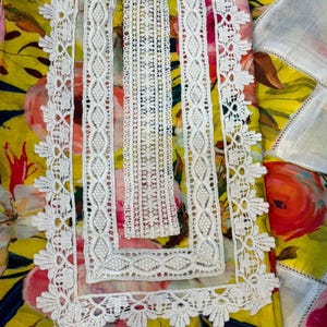 May include: Close-up of a floral patterned garment with a yellow background and pink and red flowers. The neckline and edges are trimmed with white lace. The lace has a detailed, openwork design.