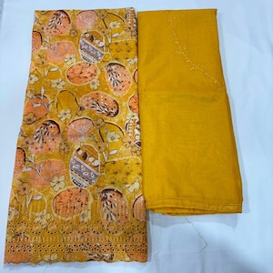 May include: A folded fabric set featuring a mustard yellow textile with a repeating pattern of orange and brown oval shapes, floral motifs, and a scalloped eyelet border, paired with a solid mustard yellow fabric with delicate embroidery.