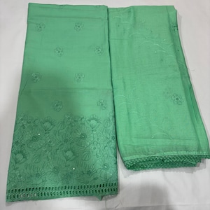 May include: A light green fabric set featuring two pieces of textile. One piece displays a dense floral embroidery pattern at the bottom edge with cutwork, while the other piece shows a sparse floral vine embroidery and a scalloped lace border.