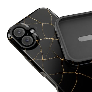 May include: Black phone case with a gold crackle design. The case has a glossy finish and features a triple-lens camera cutout. A separate black case component is visible.