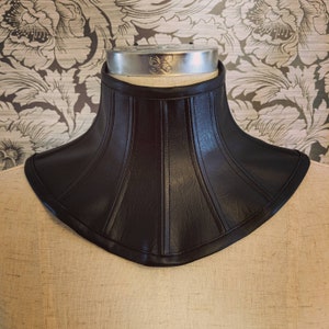 May include: A black leather choker with a wide, flared design and a smooth, textured surface.