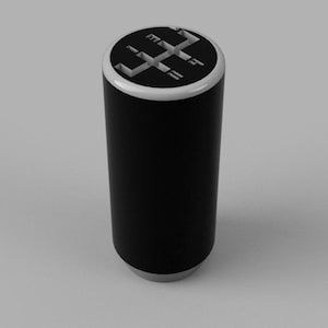 Pode incluir: Um botão de mudança de marcha cilíndrico preto com uma moldura branca. A parte superior do botão apresenta um diagrama de um padrão de engrenagem de transmissão manual de seis velocidades em preto e branco.