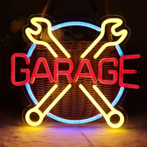 Pode incluir: Uma placa de néon com a palavra "GARAGE" em vermelho, rodeada por um círculo azul e chaves inglesas amarelas cruzadas. A placa é iluminada contra um fundo escuro, evocando uma oficina ou garagem.