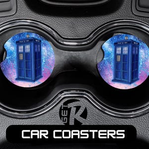 May include: Two car coasters featuring a blue police box design against a colorful galaxy background. The coasters are round and fit into a car's cup holders. The text "CAR COASTERS" is displayed on a black bar.