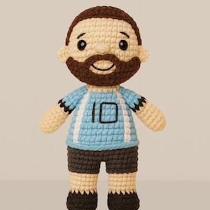 May include: A handmade crochet doll of a footballer. The doll has a light blue jersey with white stripes and the number 10. The doll has brown hair and a beard, and is wearing dark grey shorts and black shoes.