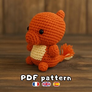 Peut inclure: Charmander en crochet orange avec des yeux noirs et un ventre crème. La queue est faite de fil orange et crème. Le texte "PDF pattern" est visible en bas de l'image.