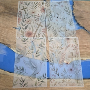 May include: Four rectangular sheets of translucent vellum paper featuring printed designs. One sheet shows crosses and wildflowers, another depicts two lambs, a third displays white doves, and the fourth features a cross with floral foliage.