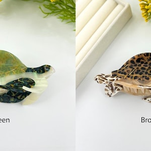 May include: Two decorative turtle figurines. One is green and white, the other is brown with a spotted pattern. The figurines are on a white surface. The word "SILENT" is in the upper left corner.