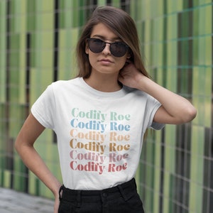 May include: White t-shirt with the text "Codify Roe" repeated in a stacked design. The text is in a variety of pastel colors.