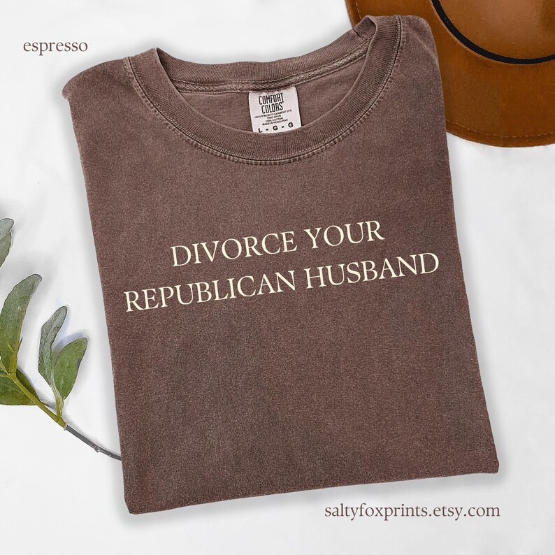 Puede incluir: Una camiseta marr&oacute;n con el texto "DIVORCE YOUR REPUBLICAN HUSBAND" impreso en blanco.