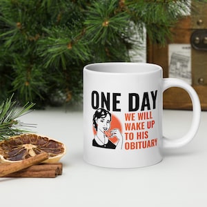 Könnte beinhalten: Eine weiße Keramik-Kaffeetasse mit einem schwarzen und roten Design. Die Tasse zeigt eine Retro-Illustration einer Frau, die aus einer Teetasse trinkt. Der Text auf der Tasse lautet "One Day We Will Wake Up To His Obituary."
