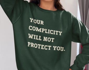 May include: A dark green sweatshirt with the text "YOUR COMPLICITY WILL NOT PROTECT YOU." printed in white.