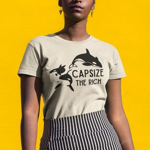 May include: A beige t-shirt with a black graphic of three orcas and the text "Capsize the Rich".