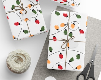 May include: Three wrapped gifts with white paper featuring a colorful string light pattern. Each package is tied with twine and a decorative tag. A ball of twine, scissors, and blank tags are also visible.