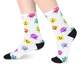 Könnte beinhalten: Weiße Socken mit einem sich wiederholenden Muster aus bunten Cartoon-Monstern in Pink, Gelb, Grün, Orange, Lila und Blau. Die Socken haben einfarbige schwarze Fersen und Zehenbereiche, wobei jedes Monster individuelle Gesichtsausdrücke zeigt.