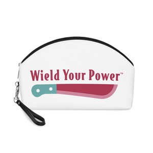 May include: White cosmetic bag with a black zip and wrist strap. The bag features the text "Wield Your Power" in burgundy, along with a cartoon machete in shades of red and teal.