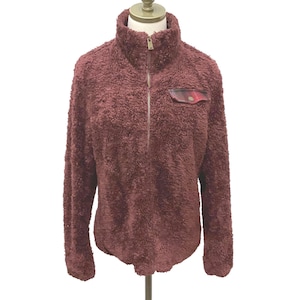 Puede incluir: Un jersey de forro polar burdeos con cuello alto y cremallera de un cuarto. El jersey tiene un pequeño bolsillo con un estampado de cuadros rojos y negros. La tela suave y texturizada se muestra en un maniquí sobre un fondo blanco.