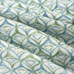 May include: Close-up of a fabric with a repeating geometric pattern. The design features diamond shapes in shades of blue and green, set against a white background. The fabric is folded, showing the texture and depth of the material.