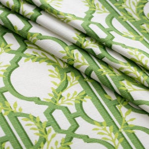 May include: Close-up of a folded fabric with a repeating trellis pattern in shades of green. The design includes stylized leaves and vines against a white background. The fabric has a textured appearance, suggesting a linen or cotton blend.