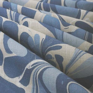 May include: Close-up of folded fabric with a marbled pattern in shades of blue and off-white. The fabric has a textured appearance, with the pattern resembling flowing water or abstract shapes. The folds create depth and dimension.