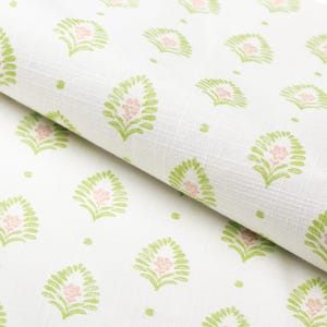 May include: White fabric with a repeating pattern of green leaf-like shapes surrounding a pink flower. The fabric is folded, showing the pattern and texture. Small green dots are scattered throughout the design.