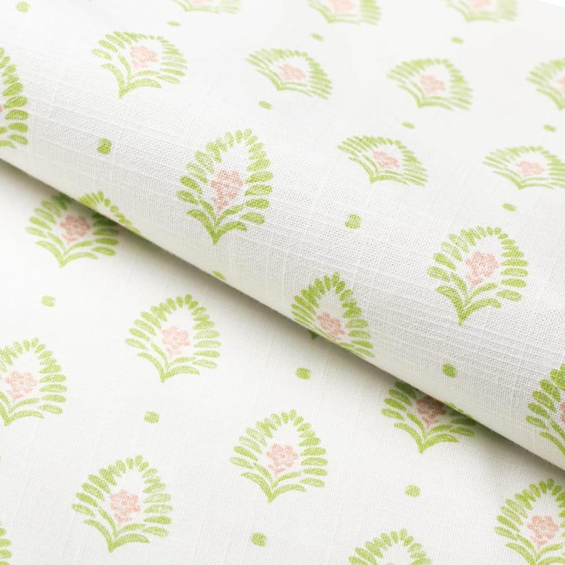 K&ouml;nnte beinhalten: Wei&szlig;er Stoff mit einem sich wiederholenden Muster aus gr&uuml;nen blattartigen Formen, die eine rosa Blume umgeben. Der Stoff ist gefaltet und zeigt das Muster und die Textur. Kleine gr&uuml;ne Punkte sind &uuml;ber das Design verstreut.