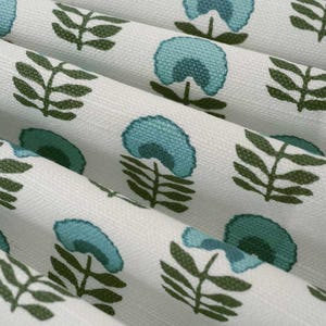 May include: Close-up of white fabric with a repeating pattern of teal-colored floral and leaf designs. The fabric is folded, showing the texture and detail of the print. The floral elements have a stylized, rounded shape.