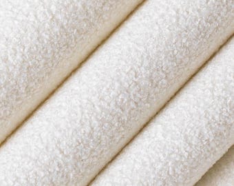 May include: Close-up of folded, off-white fabric with a textured, nubby surface. The fabric is arranged in diagonal folds, creating a sense of depth and highlighting the material's unique texture. The color is a warm, creamy white.