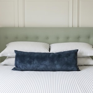 May include: A sage green upholstered headboard with button tufting, paired with two white pillows featuring thin vertical grey stripes and a long, rectangular navy blue velvet bolster pillow resting in front of the bed.