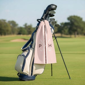 Personalizable golf towel featuring custom initials with crossed golf clubs design, displayed on a golf cart at the course. This personalized golf towel makes a thoughtful gift for golfers, golf dads, groomsmen, and tournament players, combining classic style with functional golf accessories.