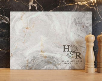 以下が含まれることがあります： 大理石模様の長方形まな板。イニシャル「H & R」、名前「Henry and Rose」、日付「2022年5月23日」がプリントされています。右側には木製の塩コショウ挽きが2つあります。