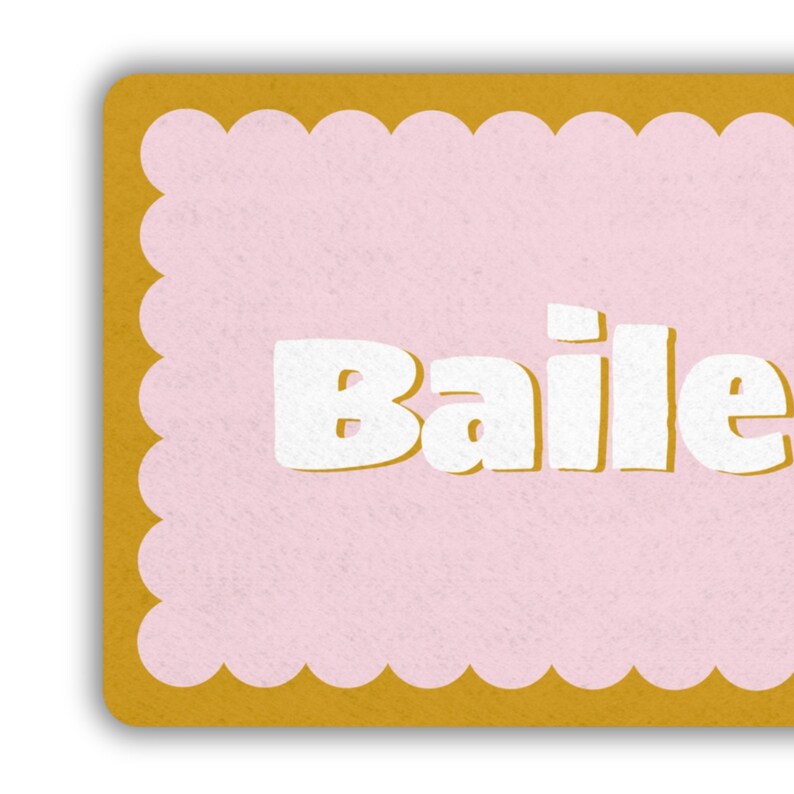 May include: A rectangular card with a scalloped edge. The card has a light pink center with the word "Baile" in bold white letters. The border is a golden yellow color.
