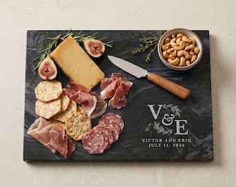 以下が含まれることがあります： チーズ、クラッカー、イチジク、サラミなどの食品が乗った長方形の黒い大理石のサービングボード。カシューナッツの小鉢とナイフも付いています。「V & E」と日付「2026年7月11日」が刻印されています。