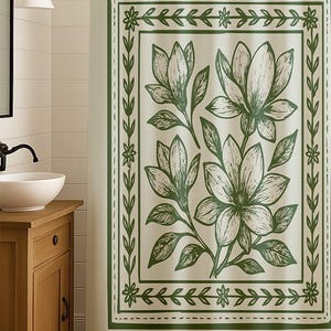 May include: A cream-colored shower curtain with a green floral design. The design features large magnolia flowers and leaves within a green border. The curtain is hanging in a bathroom setting, with a wooden vanity and a white sink visible.