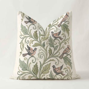 May include: A square throw pillow featuring an off-white background with a repeating pattern of stylized birds in shades of brown and gray, intertwined with scrolling green foliage and leafy vines that cover the entire surface of the fabric.