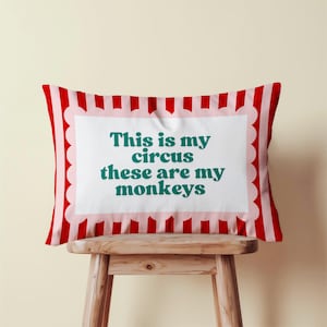 May include: A rectangular cushion with a red and white striped design. The cushion has a white, scalloped border around a white rectangle with the teal text: "This is my circus these are my monkeys".