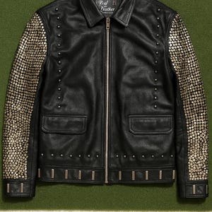 May include: Black leather jacket with silver-toned embellishments on the sleeves and studs along the seams. The jacket has a zipper closure, two front pockets, and the words "Real Leather" on the label.