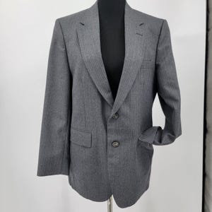 May include: A gray pinstripe blazer with two buttons and a notched lapel. The blazer has a chest pocket and two front pockets. The sleeves are cuffed. The blazer is displayed on a black mannequin.