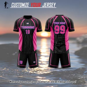 May include: A black and pink soccer jersey and shorts set featuring the text CUSTOMIZE YOUR JERSEY at the top. The jersey displays TEAMNAME 19 on the front and YOUR NAME 99 on the back. The shorts feature the number 19 in pink text.