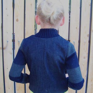 May include: A dark blue sweater with grey and black stripes on the sleeves. The sweater has a mock neck and is cropped.