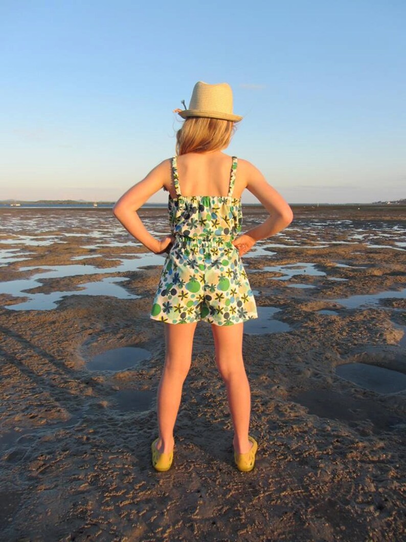 Puede incluir: Una persona joven con un sombrero de paja y un vestido de verano con estampado floral se encuentra de pie en una playa fangosa. La persona est&aacute; de espaldas a la c&aacute;mara y tiene las manos en las caderas.