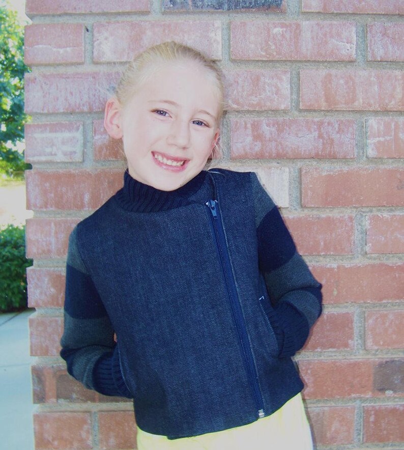 May include: A young person wearing a dark blue denim jacket with black and grey striped sleeves. The jacket has a zipper down the front and a collar.